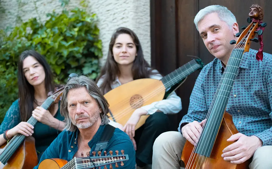 Das Ensemble Phoenix Munich mit vier Musikerinnen und Musikern auf einer Treppe im Freien, mit Viola da Gamba, Theorbe und Bassgambe vor einer Hauswand mit Begrünung.