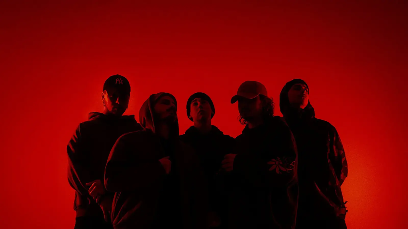 Bandfoto von Accvsed mit fünf Bandmitgliedern in dunkler Kleidung vor leuchtend rotem Hintergrund, darunter Personen mit Kapuzenpullovern, Mützen und Kappen in einer dicht stehenden Gruppenformation.