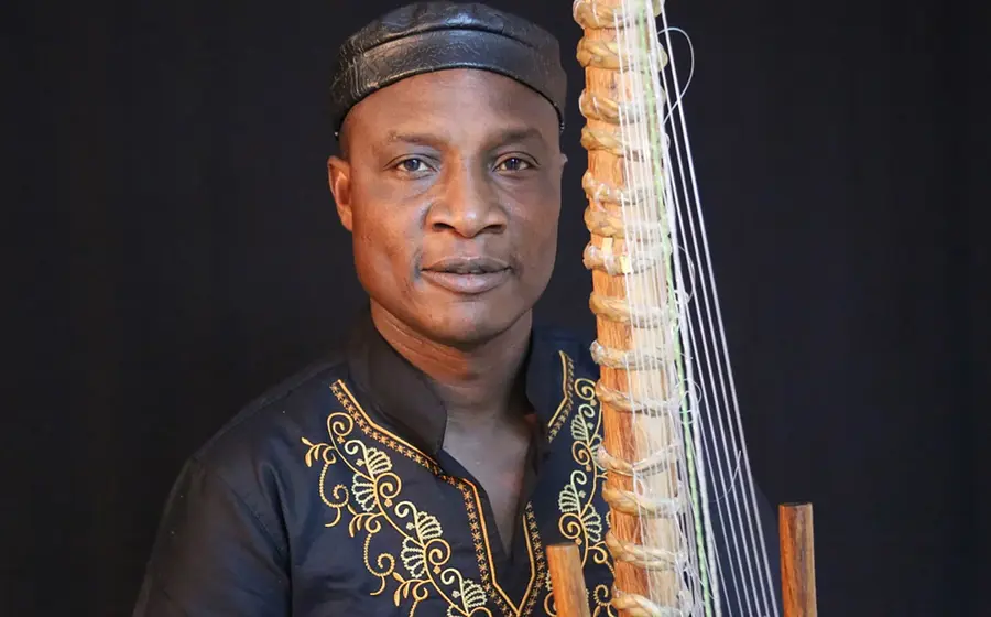 Foto für die Veranstaltung von Adjiri Odametey und Band mit dem Künstler mit einem Saiteninstrument vor schwarzem Hintergrund