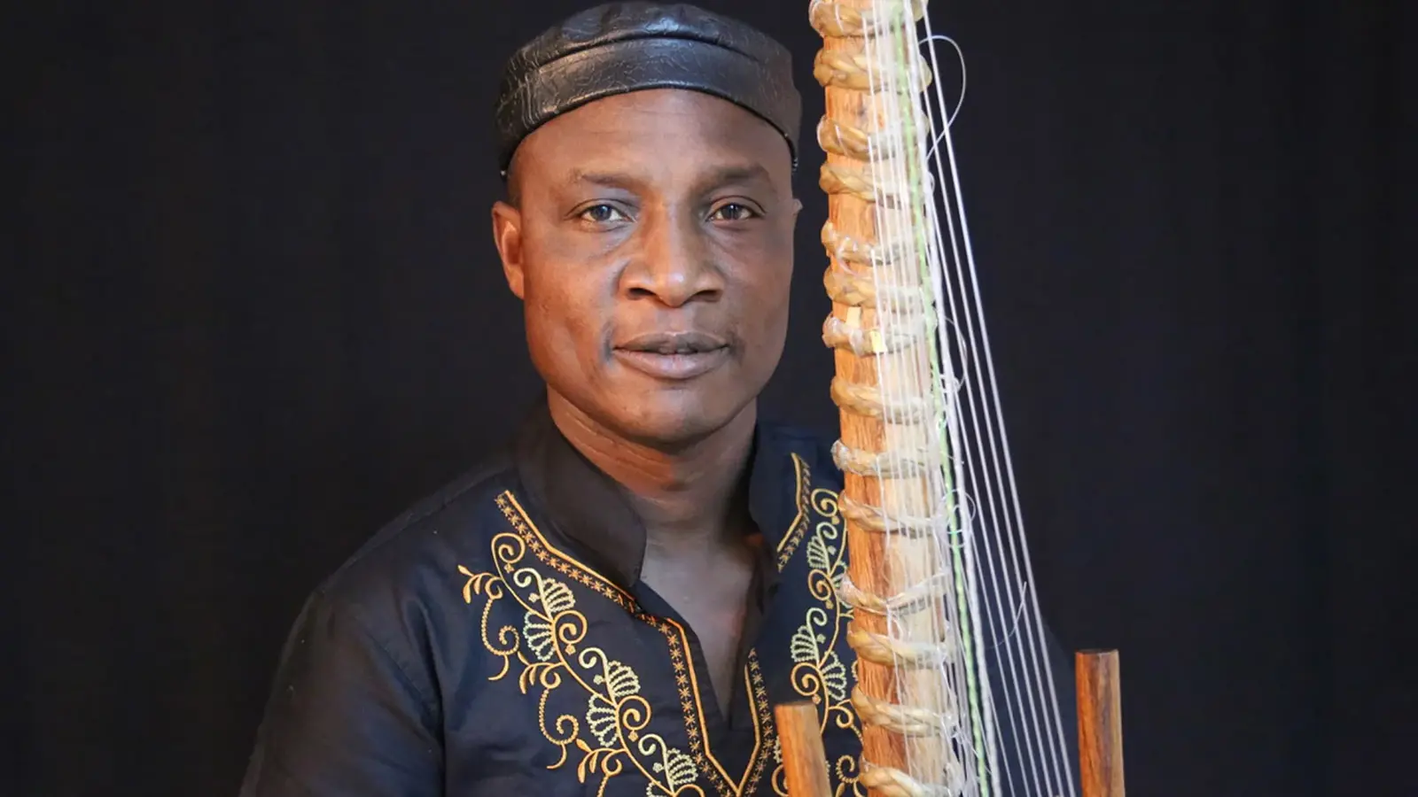 Foto für die Veranstaltung von Adjiri Odametey und Band mit dem Künstler mit einem Saiteninstrument vor schwarzem Hintergrund