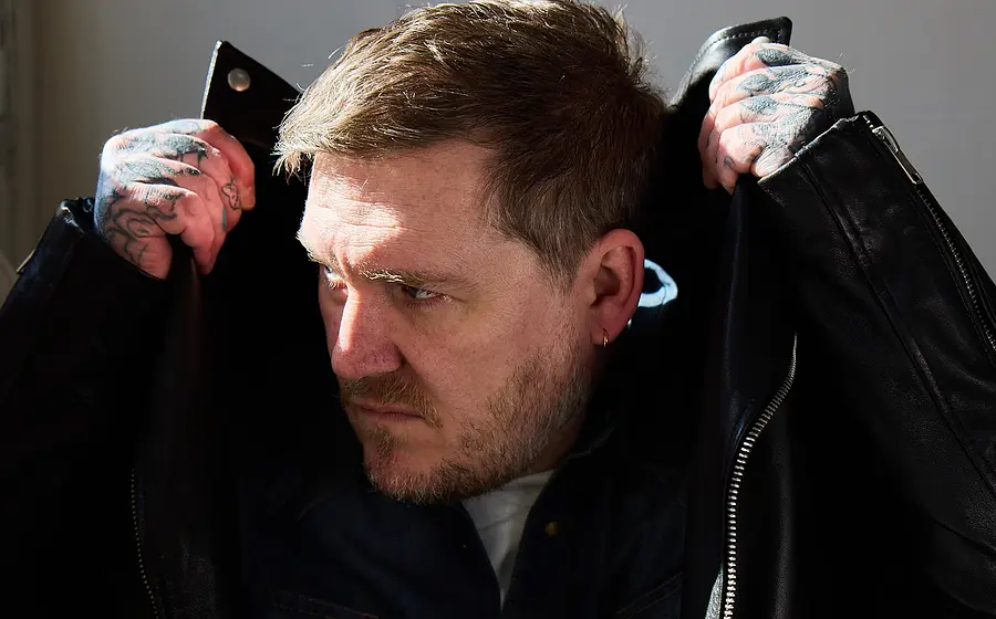 Brian Fallon mit dunkler Lederjacke, die er sich an den Kopf hochzieht, mit ernstem Blick zur Seite