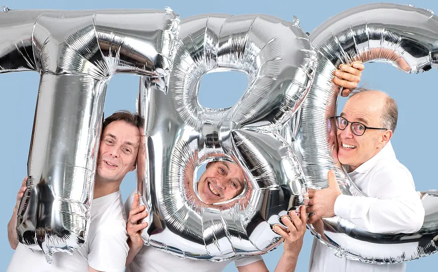Drei Männer in weißen Hemden mit den Buchstaben T,B,C als silberne Ballons