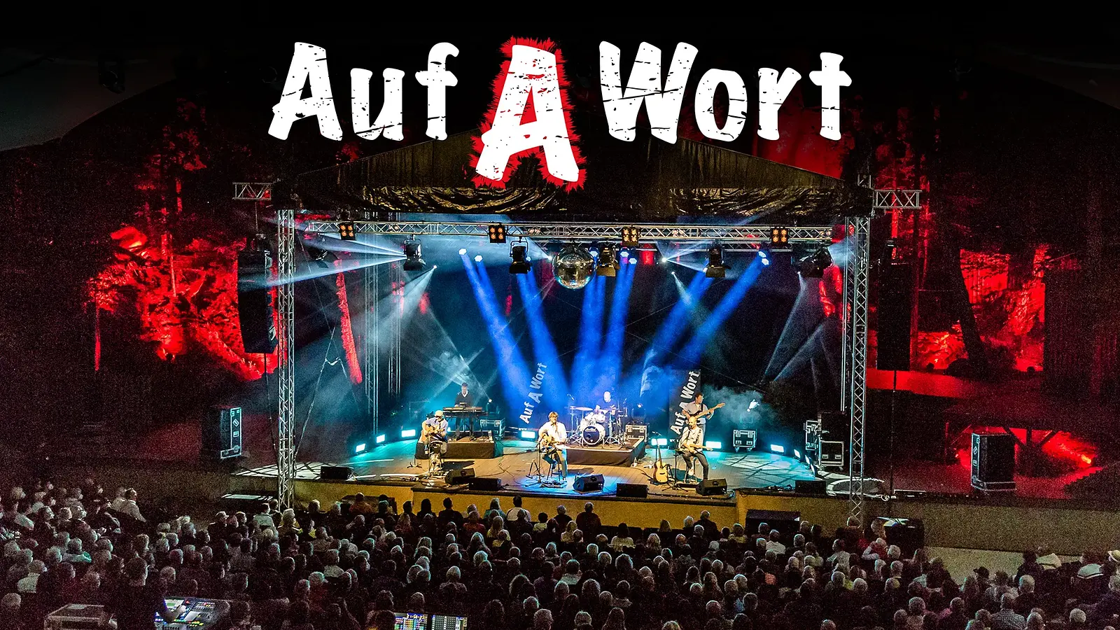 Bühnenfoto von STS mit fünf Musikern auf einer großen Open-Air-Bühne vor Publikum, beleuchtet von blauen und roten Scheinwerfern, eine Discokugel, darüber der große Schriftzug Auf A Wort