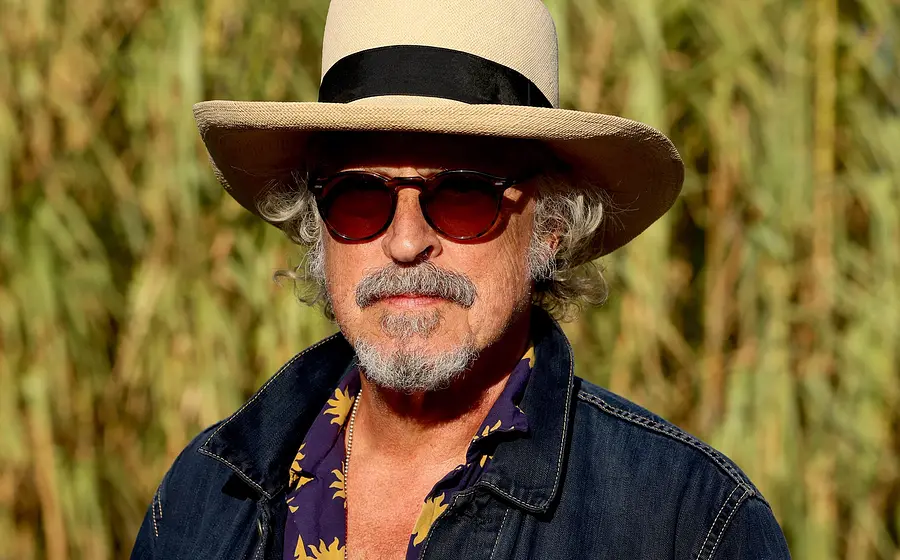 Foto des Künstlers BAP mit Hut, Sonnenbrille und Jeansjacke vor unscharfem Hintergrund.
