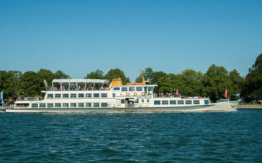 EIn Schiff mit mehreren Personen auf dem Wasser, im Hintergrund Parklandschaft