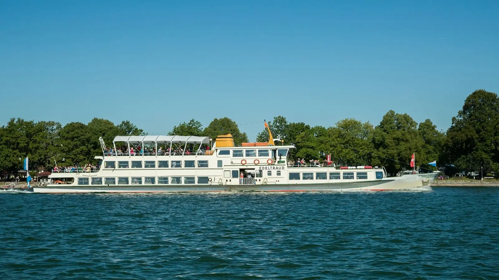 EIn Schiff mit mehreren Personen auf dem Wasser, im Hintergrund Parklandschaft