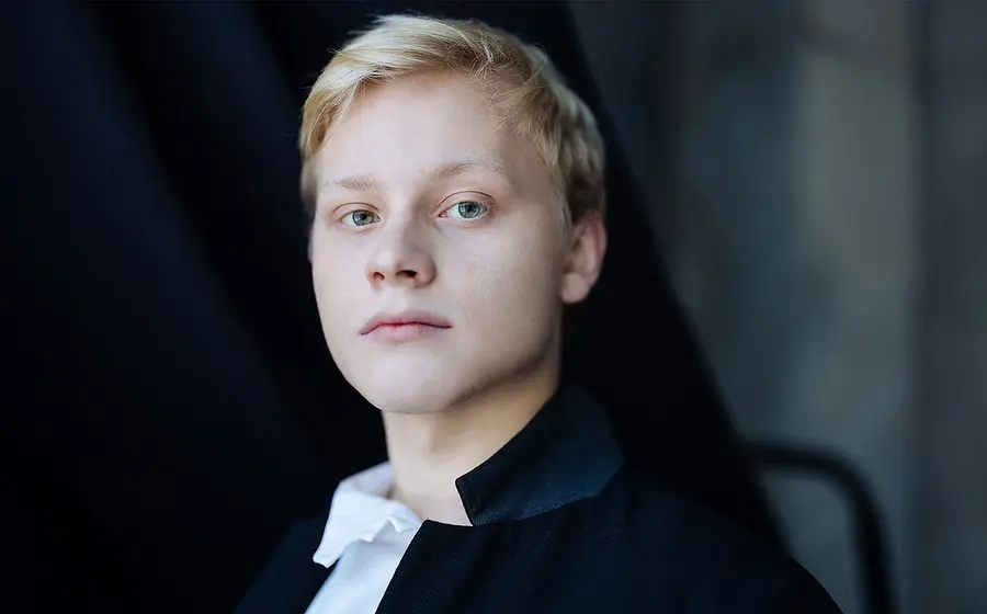 Portrait des Künstlers Alexander Malofeev in weißem Hemd und dunkler Jacke vor dunklem Hintergrund