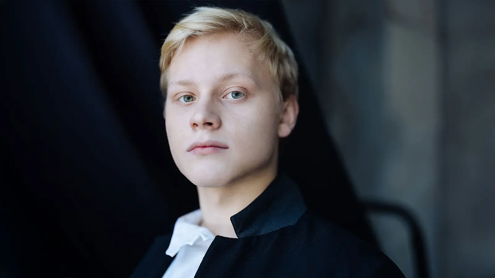 Portrait des Künstlers Alexander Malofeev in weißem Hemd und dunkler Jacke vor dunklem Hintergrund