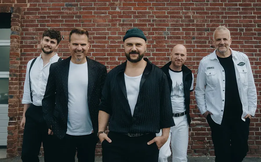Fünf Musiker in schwarz-weisser Kleidung vor einer Ziegelwand