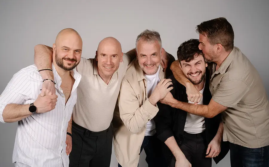 Die Mitglieder der Band Alte Bekannte stehen lachend zusammen vor hellgrauem Hintergrund