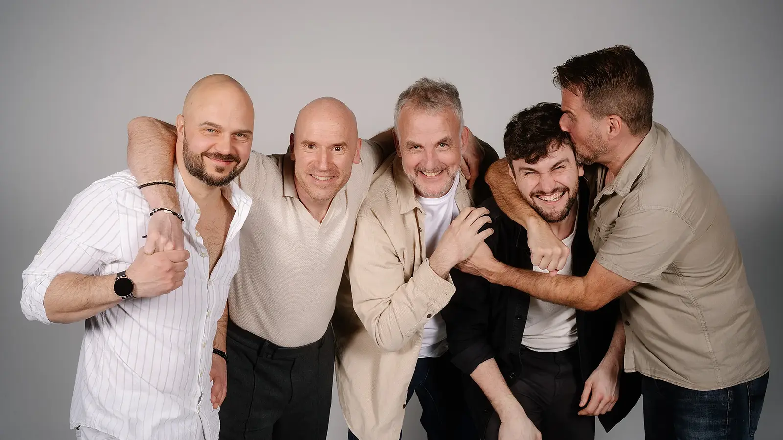 Die Mitglieder der Band Alte Bekannte stehen lachend zusammen vor hellgrauem Hintergrund