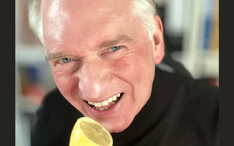 Der Kabarettist in schwarzem Pullover macht eine Grimasse und hält sich eine aufgeschnittene Zitrone an den Mund