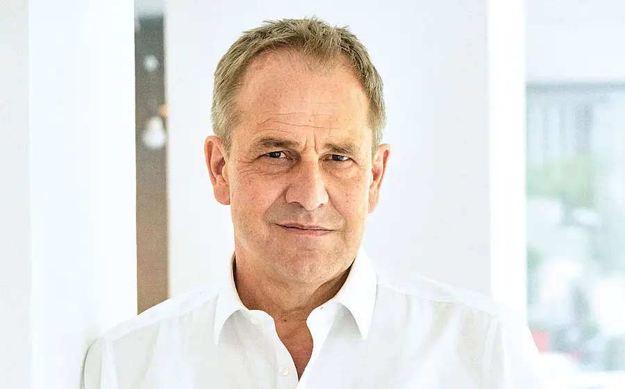 Porträt Stephan Schad in weißem Hemd, vor hellem Innenraum mit weißen Wänden und weichem Tageslicht