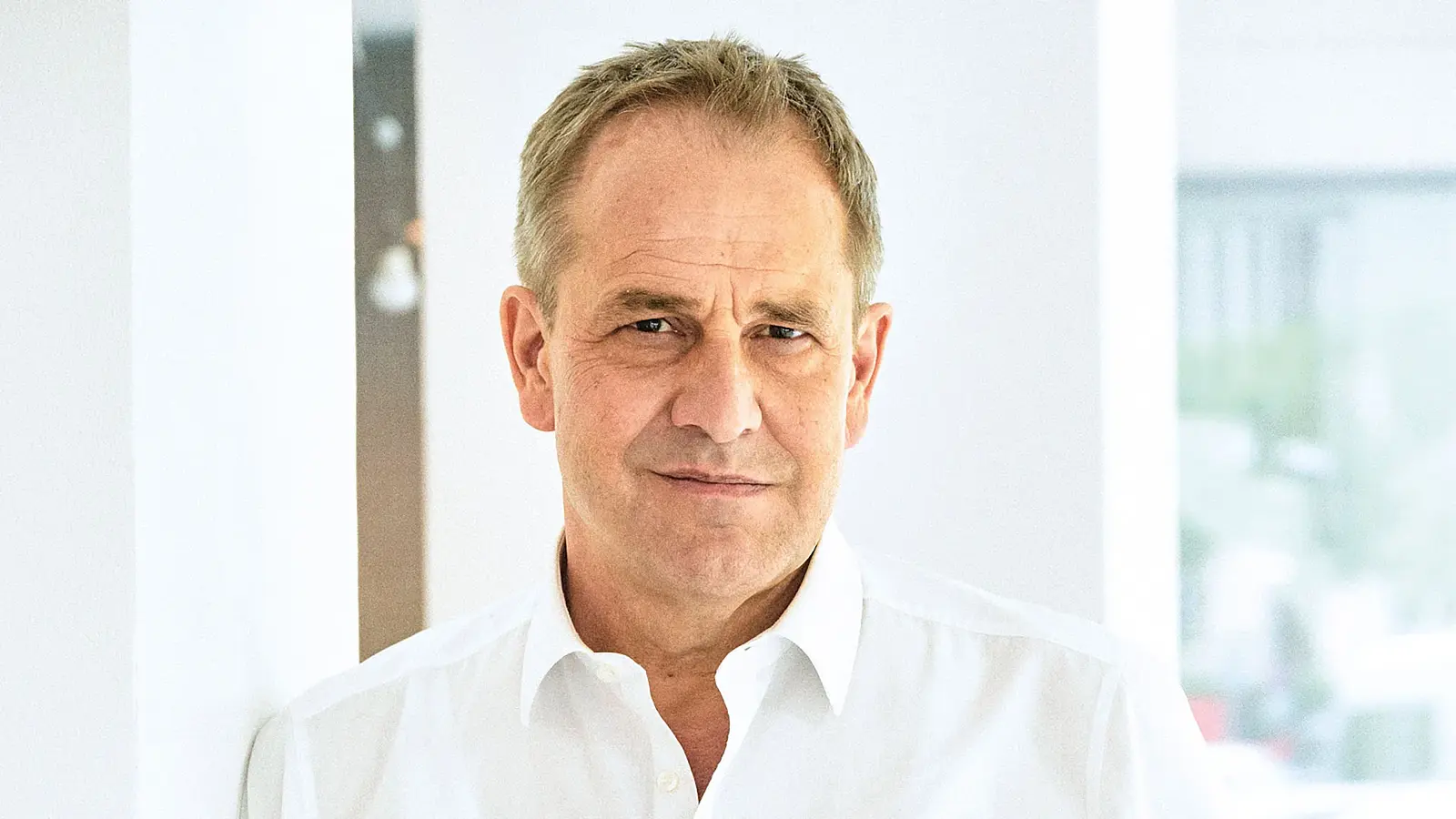 Porträt Stephan Schad in weißem Hemd, vor hellem Innenraum mit weißen Wänden und weichem Tageslicht