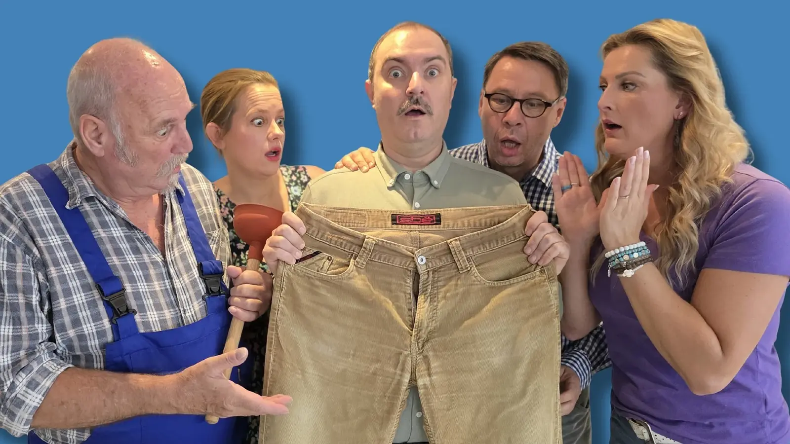 Fünf Darsteller stehen eng zusammen, eine Person hält eine beige Hose hoch, während die anderen darauf schauen, vor blauem Hintergrund