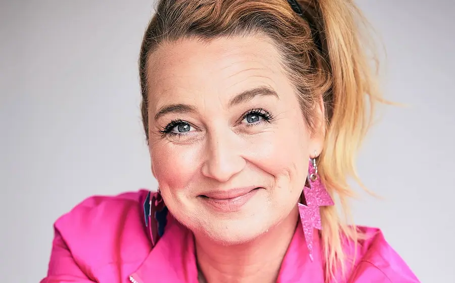 Ein Portrait von Constanze Lindner mit pinkem Oberteil und pinken Blitzförmigen Ohrringen vor weißem Hintergrund