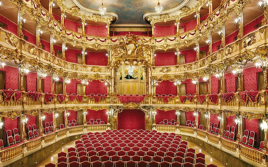 Prunkvoller Theatersaal mit roten Sitzen, roten Logen und reich verzierten goldenen Rokoko-Elementen auf mehreren Rängen. Zentraler Blick in den Zuschauerraum des Cuvilliés-Theaters.