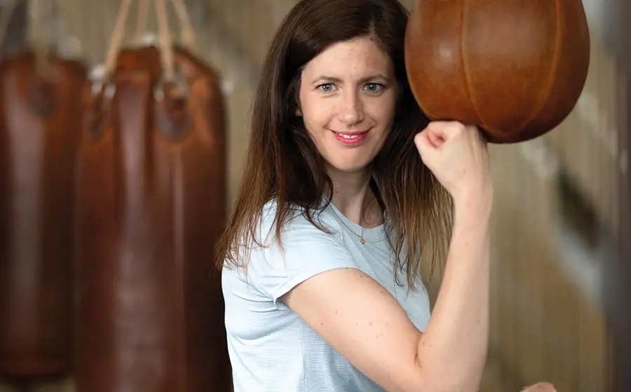 Claudia Pichler in weißem T-Shirt, die Hand zu einer Faust geballt, im Hintergrund Boxsäcke
