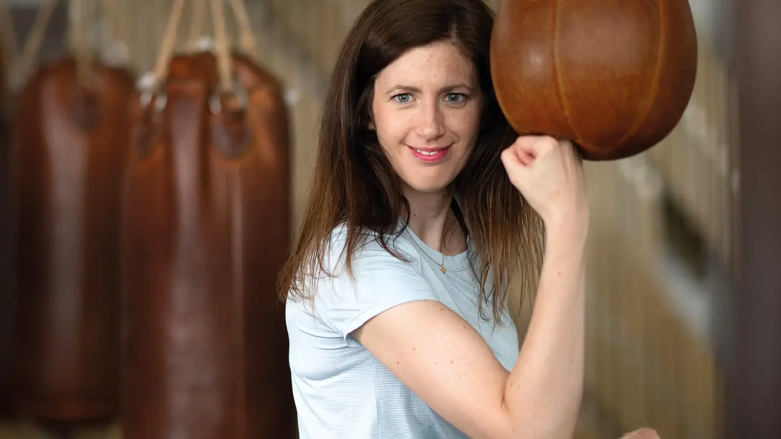 Claudia Pichler in weißem T-Shirt, die Hand zu einer Faust geballt, im Hintergrund Boxsäcke