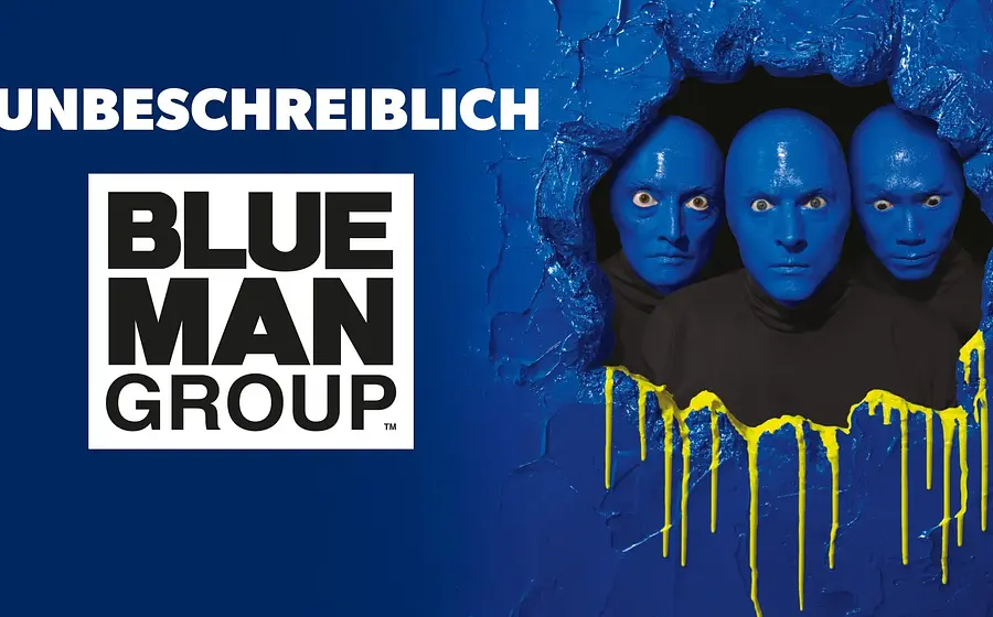 Drei blau bemalte Köpfe blicken durch eine aufgebrochene blaue Wand mit gelben Farbtropfen; links weißer Schriftzug UNBESCHREIBLICH Blue Man Group
