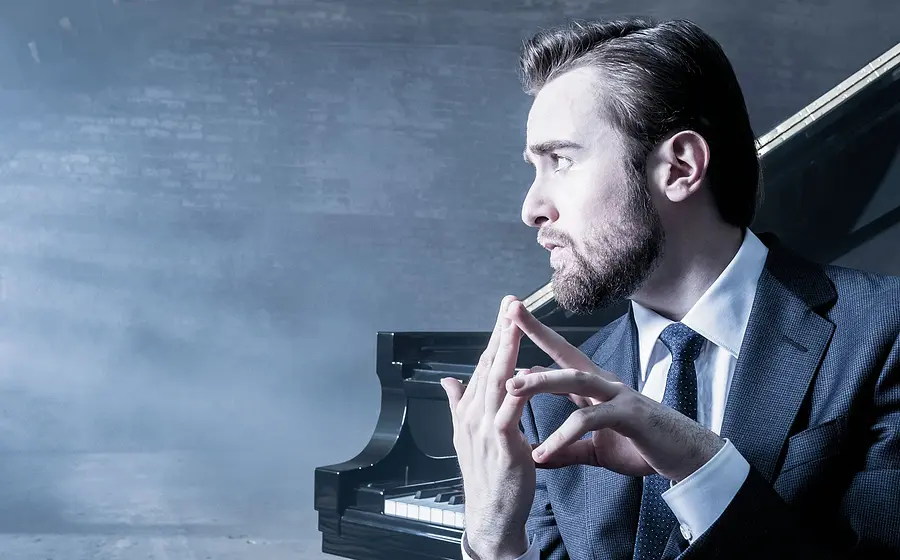 Promobild für das Event ‚Daniil Trifonov & Berliner Barocksolisten‘: Eine Person im dunklen Anzug sitzt vor einem Flügel in einem neblig beleuchteten Raum und hält die Hände vor dem Instrument