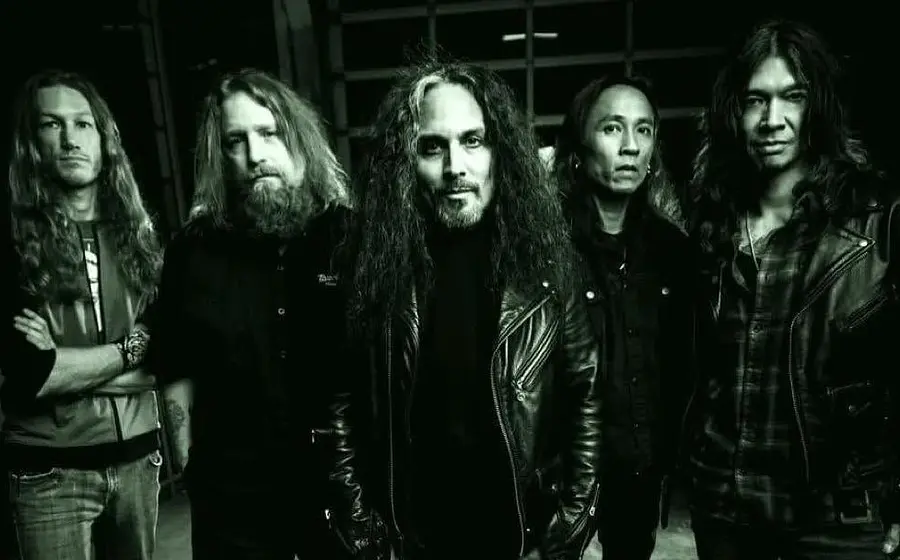 Death Angel in dunkler Kleidung posieren für ein schwarz-weißes Gruppenfoto vor einem dunklen Hintergrund.