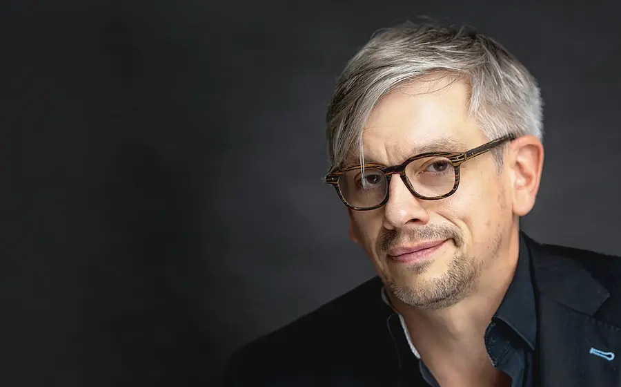 Matthias Tretter in schwarzem Hemd mit Brille vor grauem Hintergrund