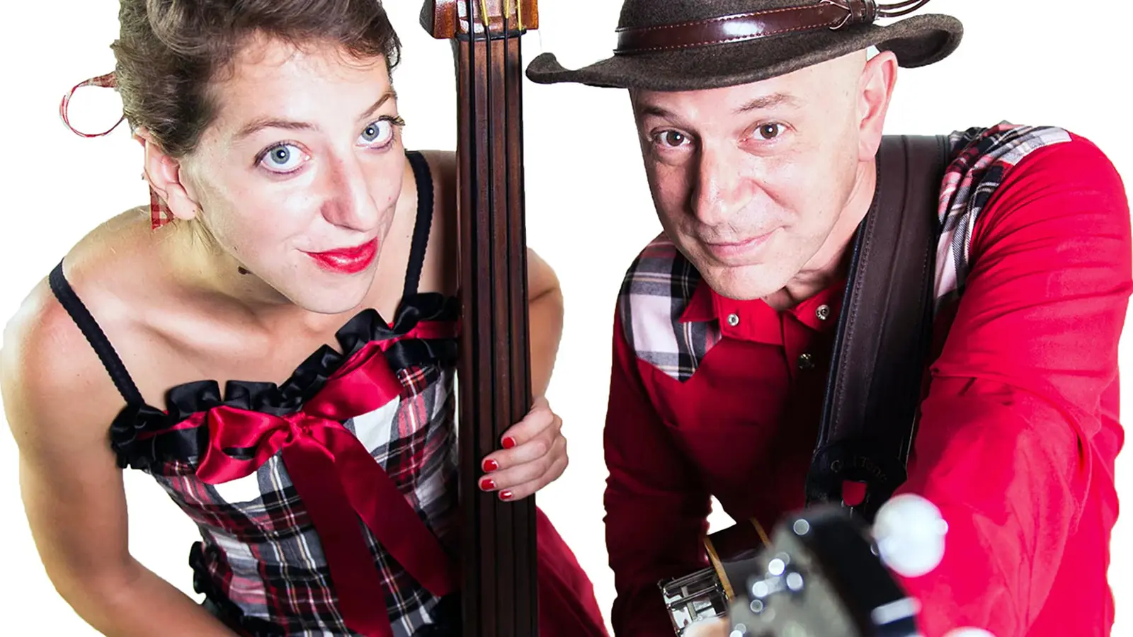 Zwei Personen im rot karierten Bühnenoutfit mit Kontrabass und Gitarre blicken in die Kamera