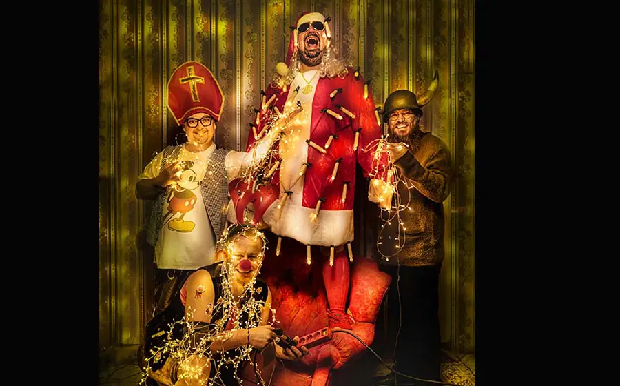 Vier Kabarettisten in weihnachtlichen Kostümen stehen und sitzen vor goldener Tapete mit Lichterketten; zentrale Figur als Nikolaus verkleidet – Werbemotiv zum Weihnachtsprogramm „O‘ghängt is!“ von Da Meier & Watschnbaam.