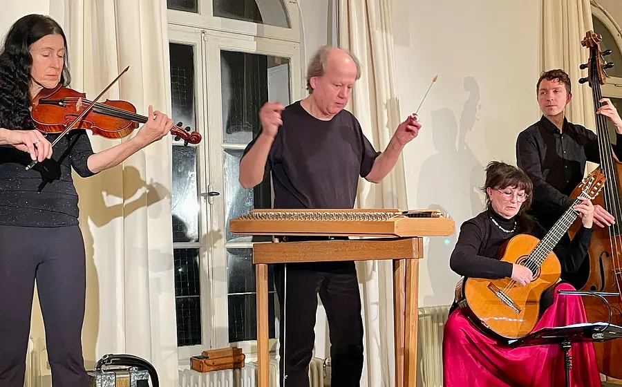 Neujahrskonzert Rudi Zapf & Freunde: Vier Musiker spielen Violine, Hackbrett, Gitarre und Kontrabass bei einem Konzert in einem Saal mit heller Innenraumkulisse.