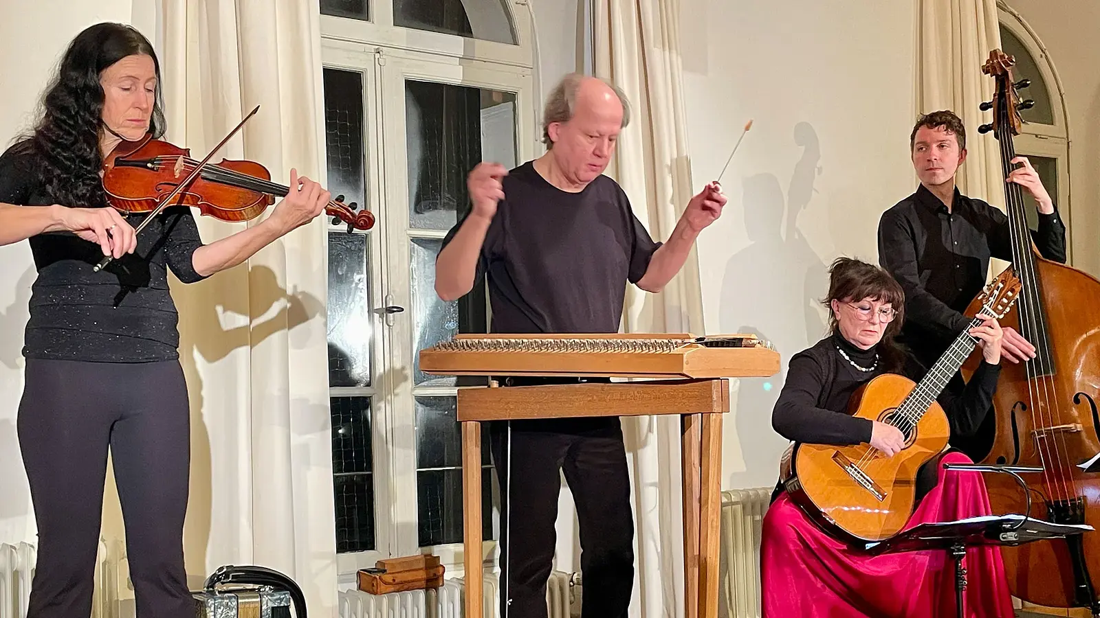 Neujahrskonzert Rudi Zapf & Freunde: Vier Musiker spielen Violine, Hackbrett, Gitarre und Kontrabass bei einem Konzert in einem Saal mit heller Innenraumkulisse.