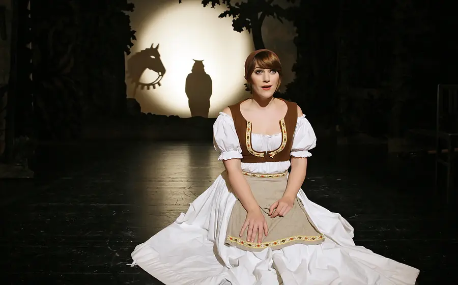Darsteller sitzt im Kostüm eines Märchenmusicals auf der Bühne, im Hintergrund eine leuchtende Kreisprojektion mit Tier-Schatten