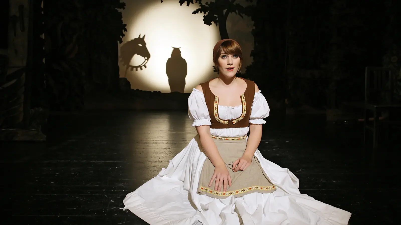 Darsteller sitzt im Kostüm eines Märchenmusicals auf der Bühne, im Hintergrund eine leuchtende Kreisprojektion mit Tier-Schatten
