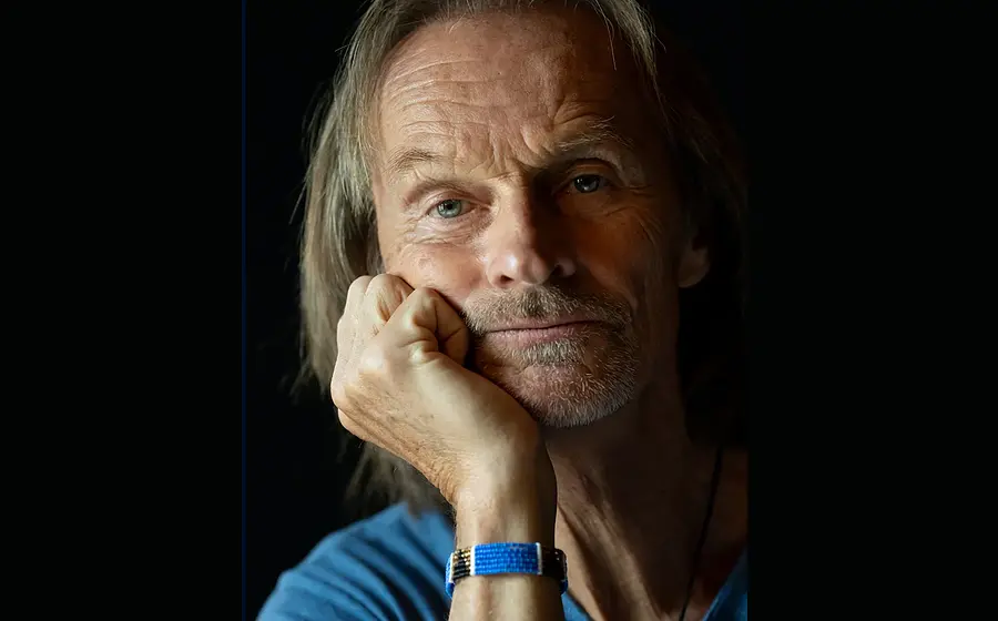 Eisi Gulp in blauem Shirt, das Kinn auf die Hand gestützt