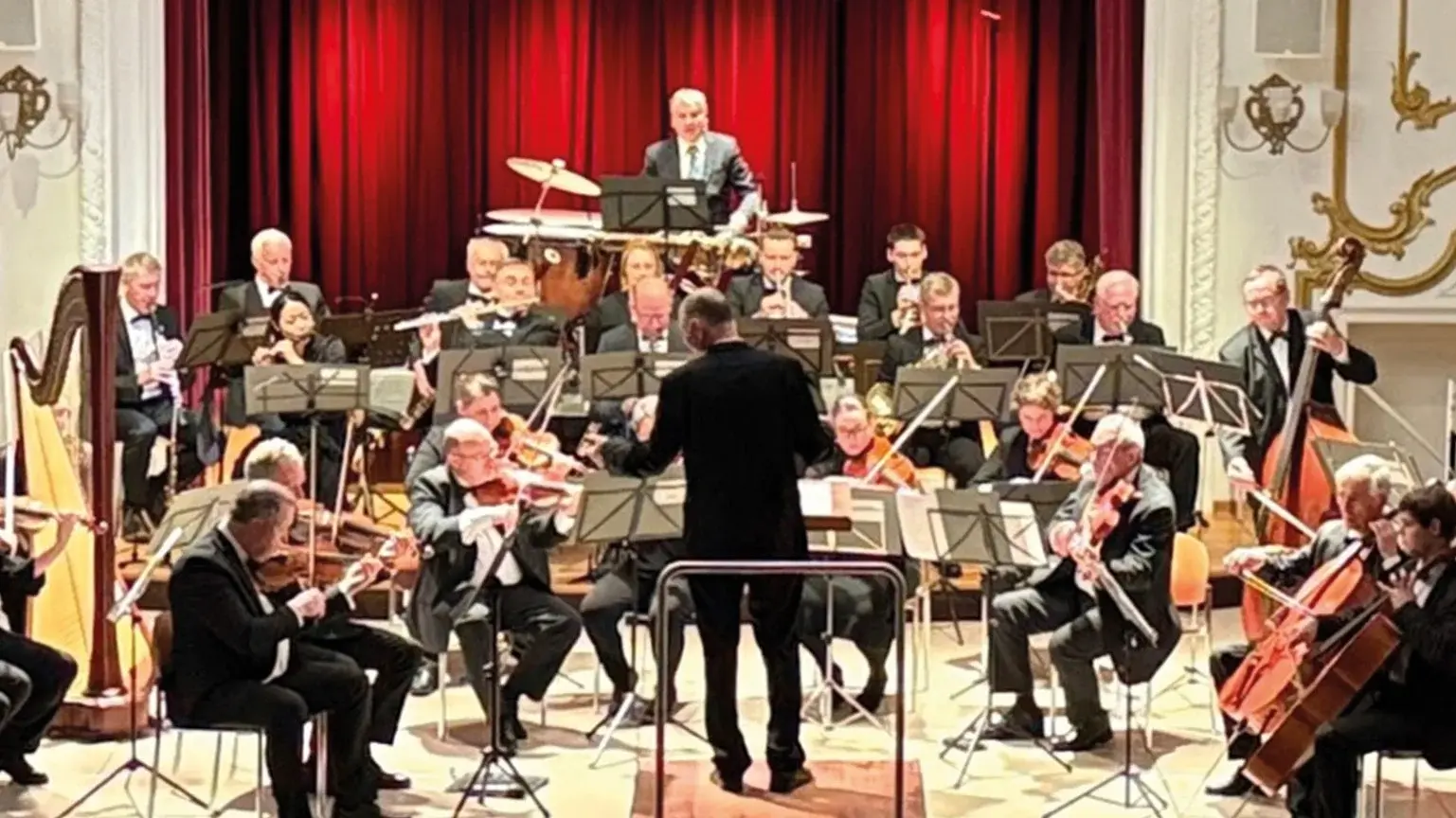 Ein Orchester auf einer Bühne vor einem roten Vorhang