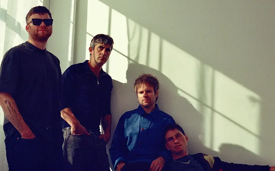 Foto für die Gruppe ENTER SHIKARI mit einem Bild der vier Künstler vor einer weißen Wand im Sonnenlicht.