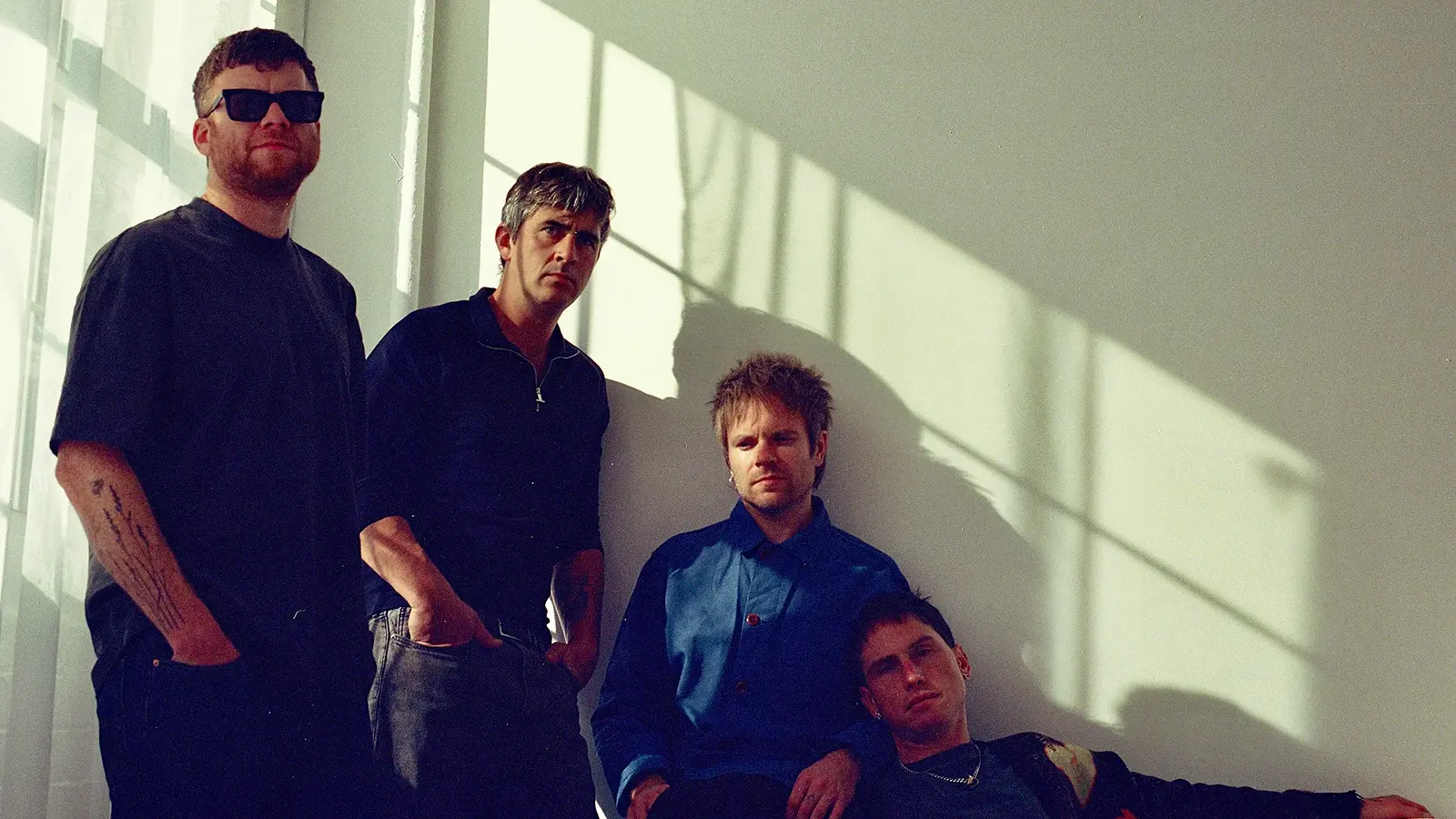 Foto für die Gruppe ENTER SHIKARI mit einem Bild der vier Künstler vor einer weißen Wand im Sonnenlicht.