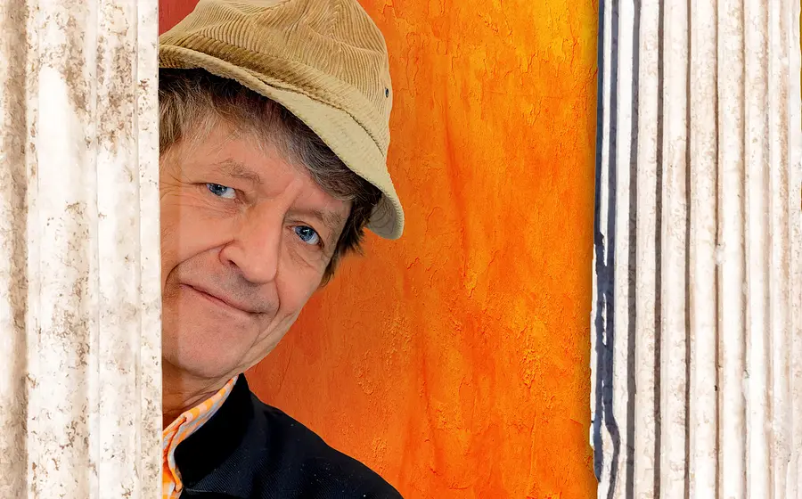 Portrait des Künstlers mit Mütze vor orangem Hintergrund
