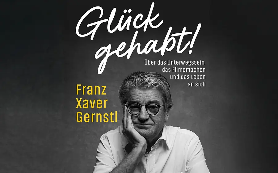 Plakat Glück gehabt! von Franz Xaver Gernstl mit Schwarzweißporträt einer Person in weißem Hemd und runder Brille, den Kopf auf eine Hand gestützt, vor dunklem Hintergrund sowie Titel und Untertitel zum Unterwegssein, Filmemachen und Leben.