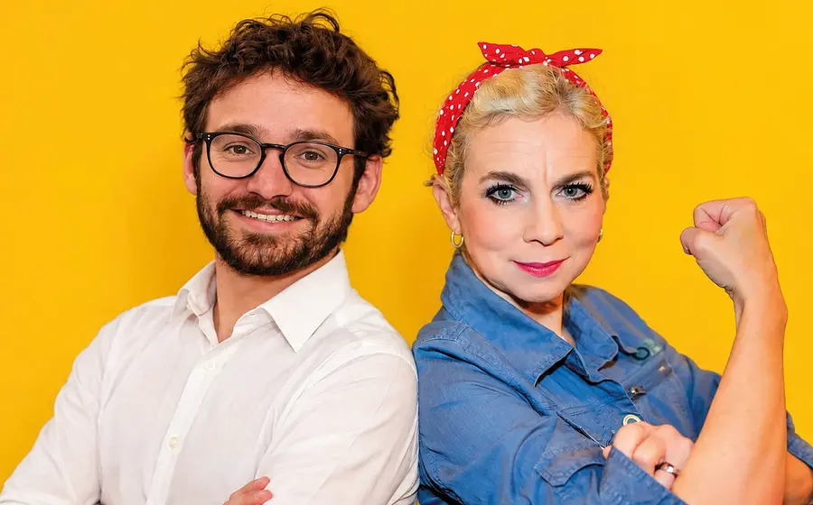 Franziska Ball und Felix Mathy stehen aneinandergelehnt, sie mit rot getupftem Kuopftuch und eine Hand zur Faust geballt, er in weißem Hemd vor gelbem Hintergrund