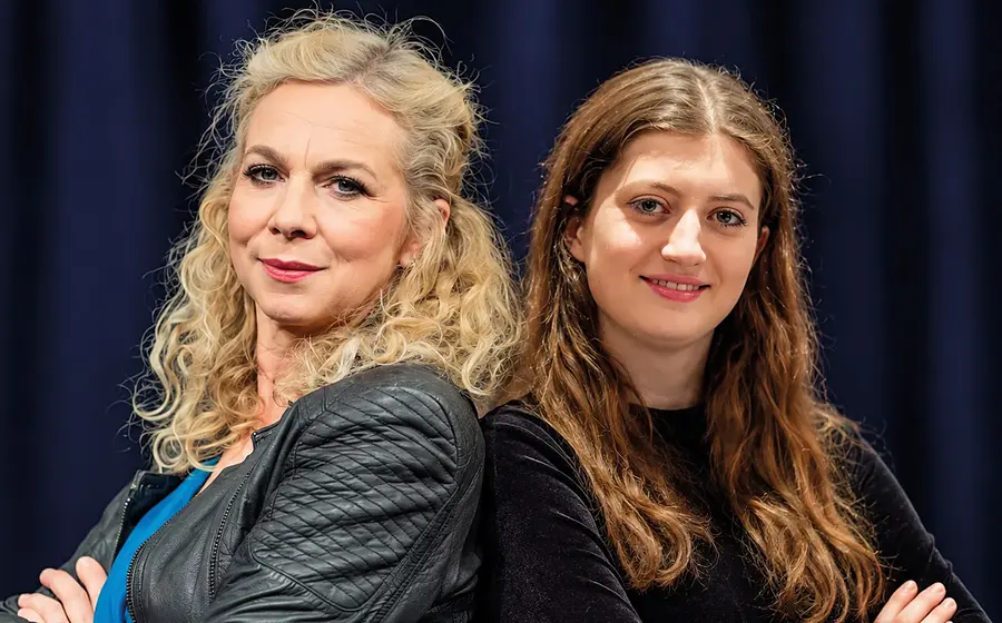 Franziska Ball und Bianca Seufert in dunkler Kleidung stehen aneinandergelehnt und blicken in die Kamera, vor dunkelblauem Hintergrund