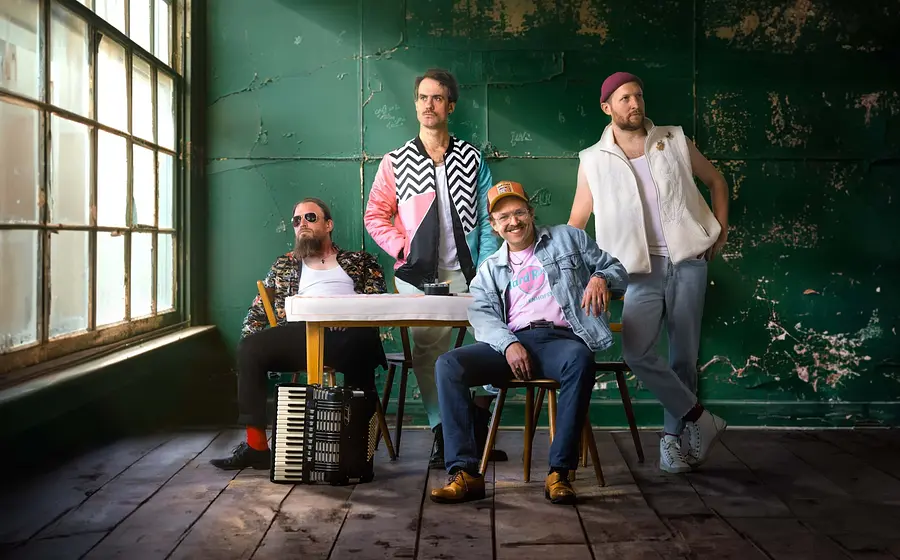 die Band Gankino Circus in einem Raum mit alten Fenstern in dunklem Licht vor einer türkisgrünen Wand