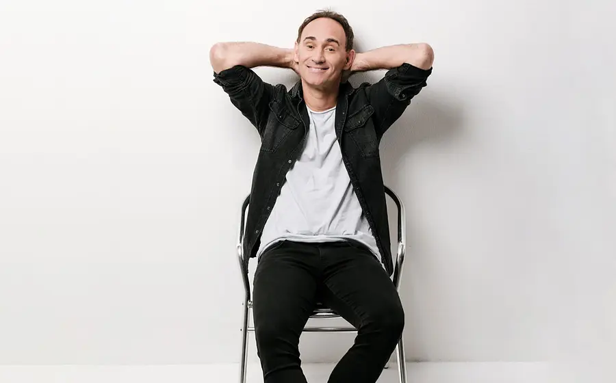 Porträt des Kabarettisten Gernot Kulis auf einem Stuhl sitzend vor hellem Hintergrund, Werbefoto zum Comedy-Programm von Gernot Kulis.