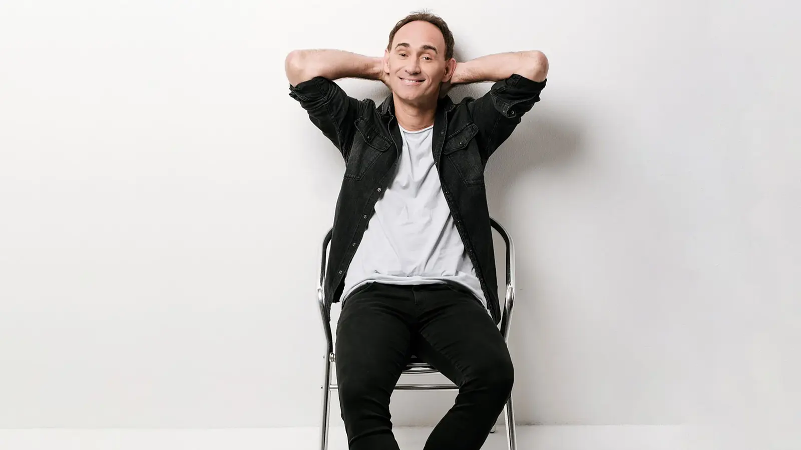 Porträt des Kabarettisten Gernot Kulis auf einem Stuhl sitzend vor hellem Hintergrund, Werbefoto zum Comedy-Programm von Gernot Kulis.