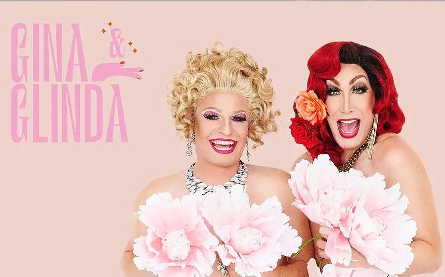Gina Colada & Glinda Glanz – zwei Travestie-Künstlerinnen mit glamourösem Styling und großen Blumen vor hellem Hintergrund, humorvolle Drag-Show im Silbersaal.