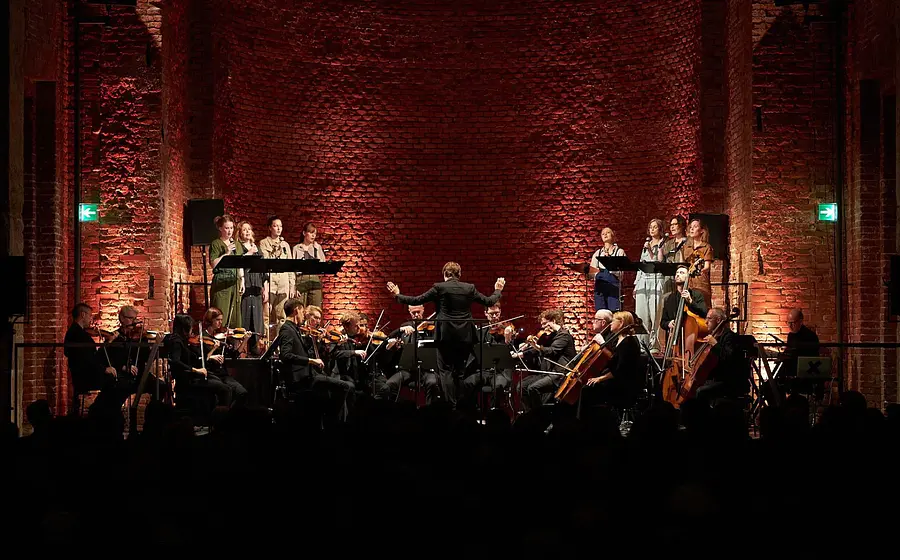 Ein Orchester vor einenr Bühnenkulisse aus rohen Ziegeln in warmem Licht