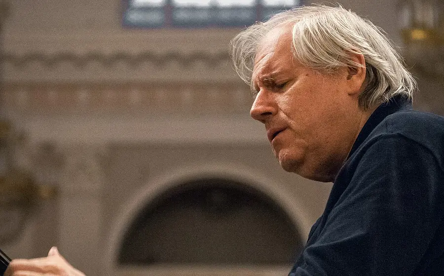 Promobild für das Event ‚Grigory Sokolov, Klavier‘: Eine Person in dunkler Kleidung sitzt an einem Flügel in einem großen Saal mit hellen Wandstrukturen und einem runden Bogen im Hintergrund