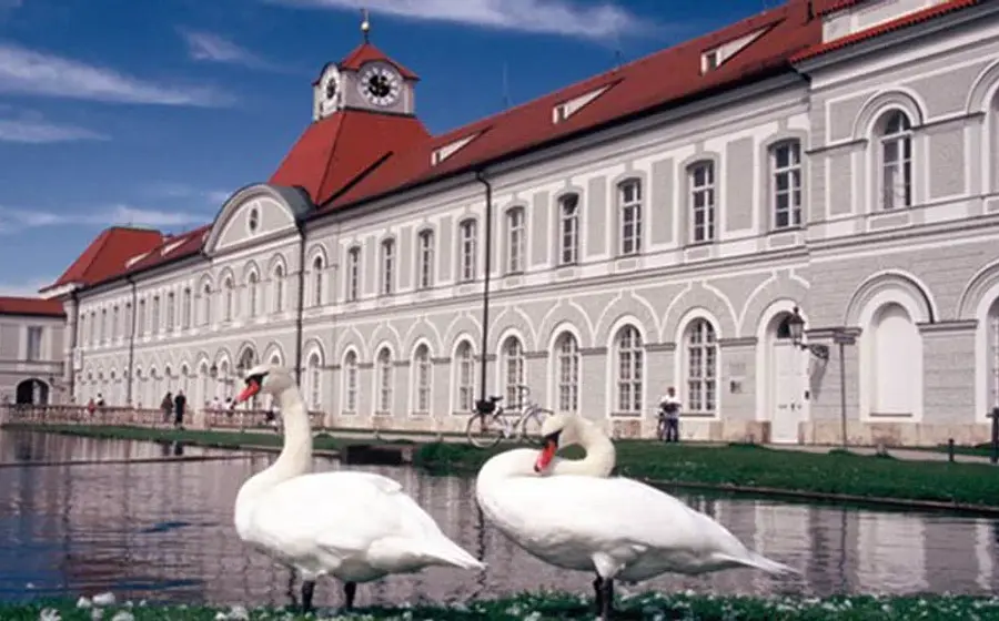 Eine Seite des Schloss Nymphenburg mit einem Teich, im Vordergrund zwei Gänse