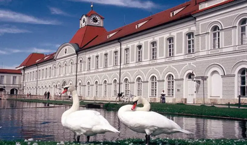 Eine Seite des Schloss Nymphenburg mit einem Teich, im Vordergrund zwei Gänse
