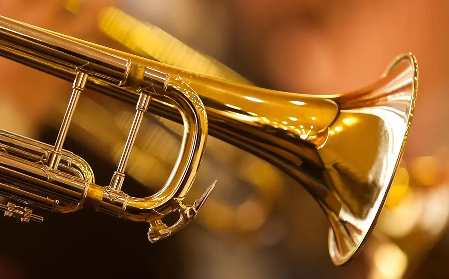 Nahaufnahme einer goldenen Trompete mit Ventilen und Schalltrichter vor warmem, unscharfem Hintergrund mit Lichteffekten in goldenen und orangefarbenen Tönen.